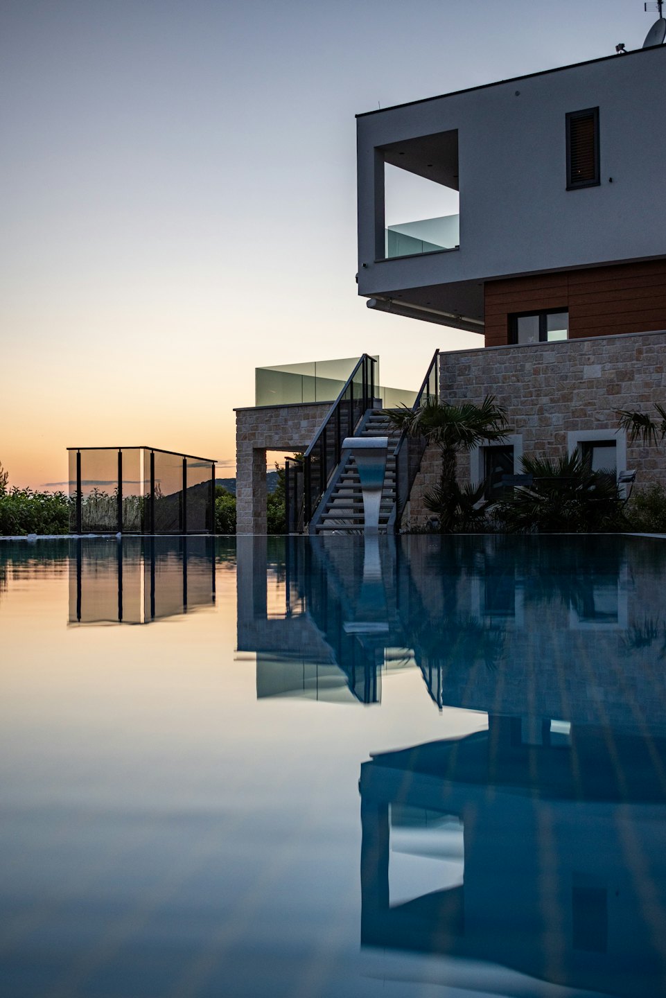Luxury house with infinity pool at sunset reflecting sky.