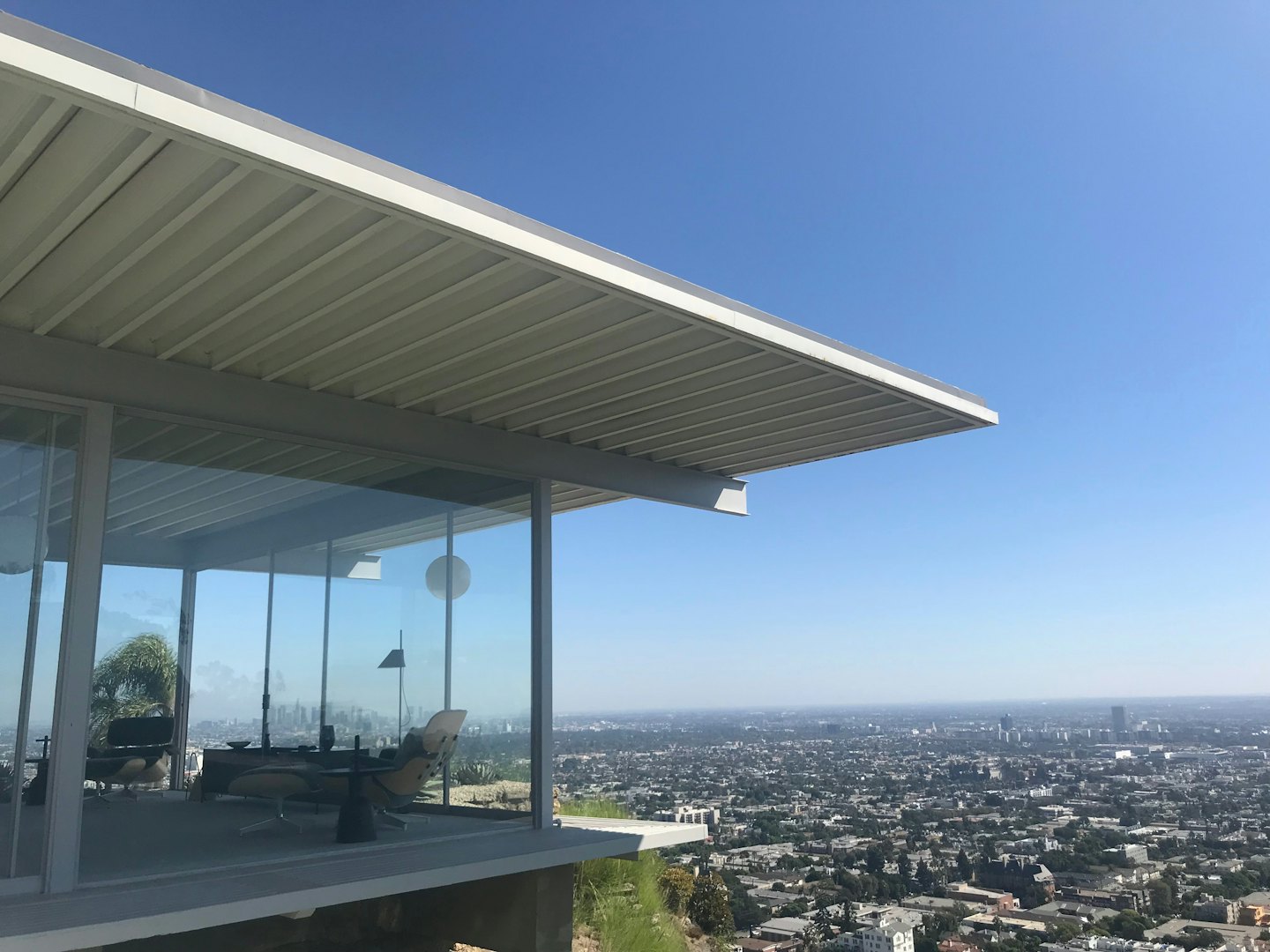 Modern glass house with cantilevered roof overlooks city skyline.